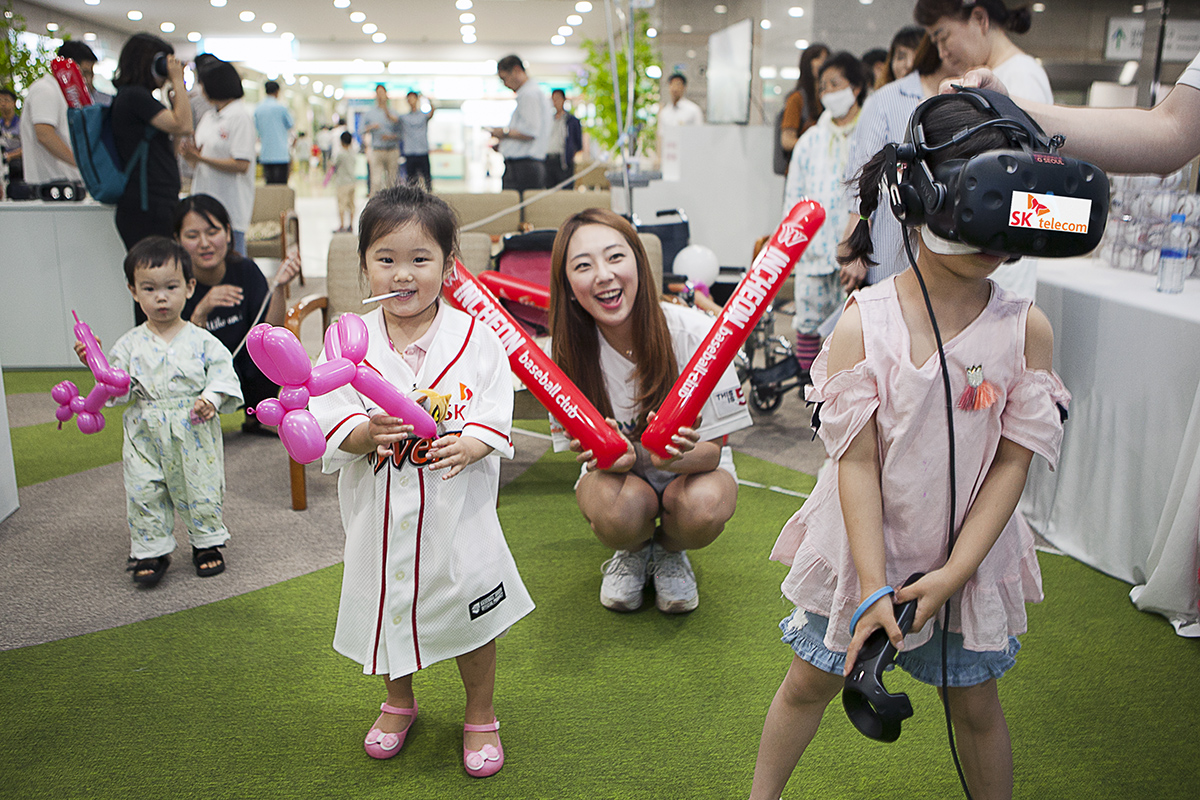 SK텔레콤이 16일 인천시 중구 인하대병원 로비에 마련한 '찾아가는 야구장'에서 어린이 환자들이 가상현실 기기를 통해 야구 게임을 즐기고 있다. /사진=SK텔레콤