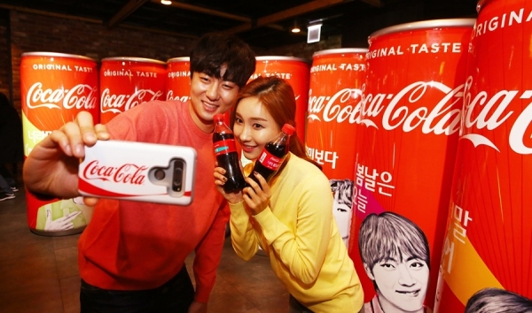 최근 출시된 코카-콜라 방탄소년단 패키지를 대형 캔을 배경으로 다정하게 셀카를 찍고 있다. 제공/코카-콜라
