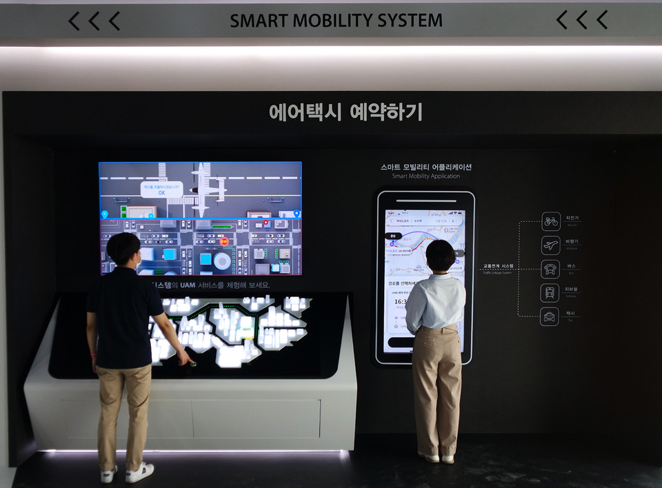 관람객들이 한화시스템 기업관에서 에어택시 모바일 앱(App) 예약을 체험해보고 있다. 현재 교통시간과 한화시스템 에어택시 ‘버터플라이’를 탑승한 소요시간을 비교 확인하는 모습 (제공=한화시스템)